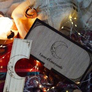 Marque-page et boucles d’oreilles Lune d’émeraude près d’un carnet ancien et de feuilles de lierre.